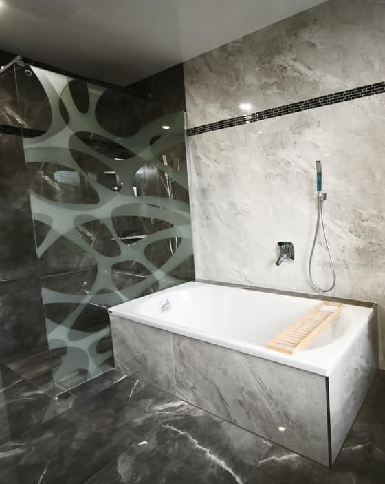 Badewanne mit Fliesenverkleidung und Glas-Trennwand mit Muster